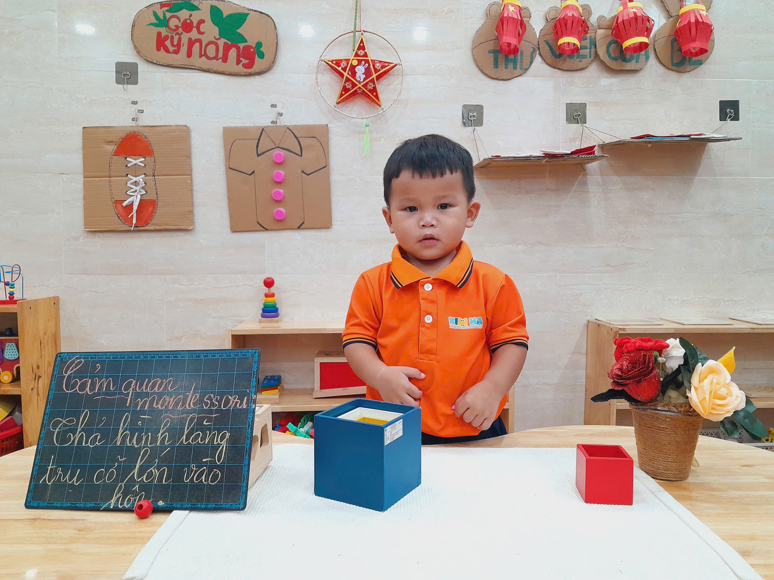 bé trai thực hành thả hình vào hộp montessori kim hà